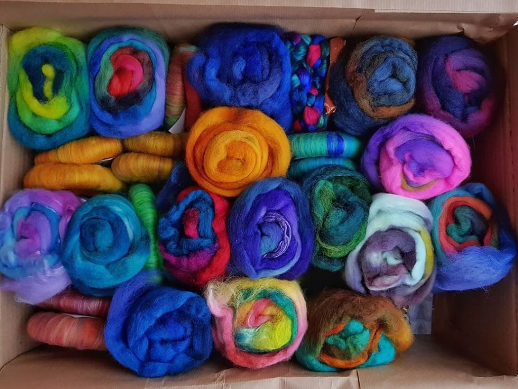 A cardboard box full of rolags and minibatts in saturated colours.