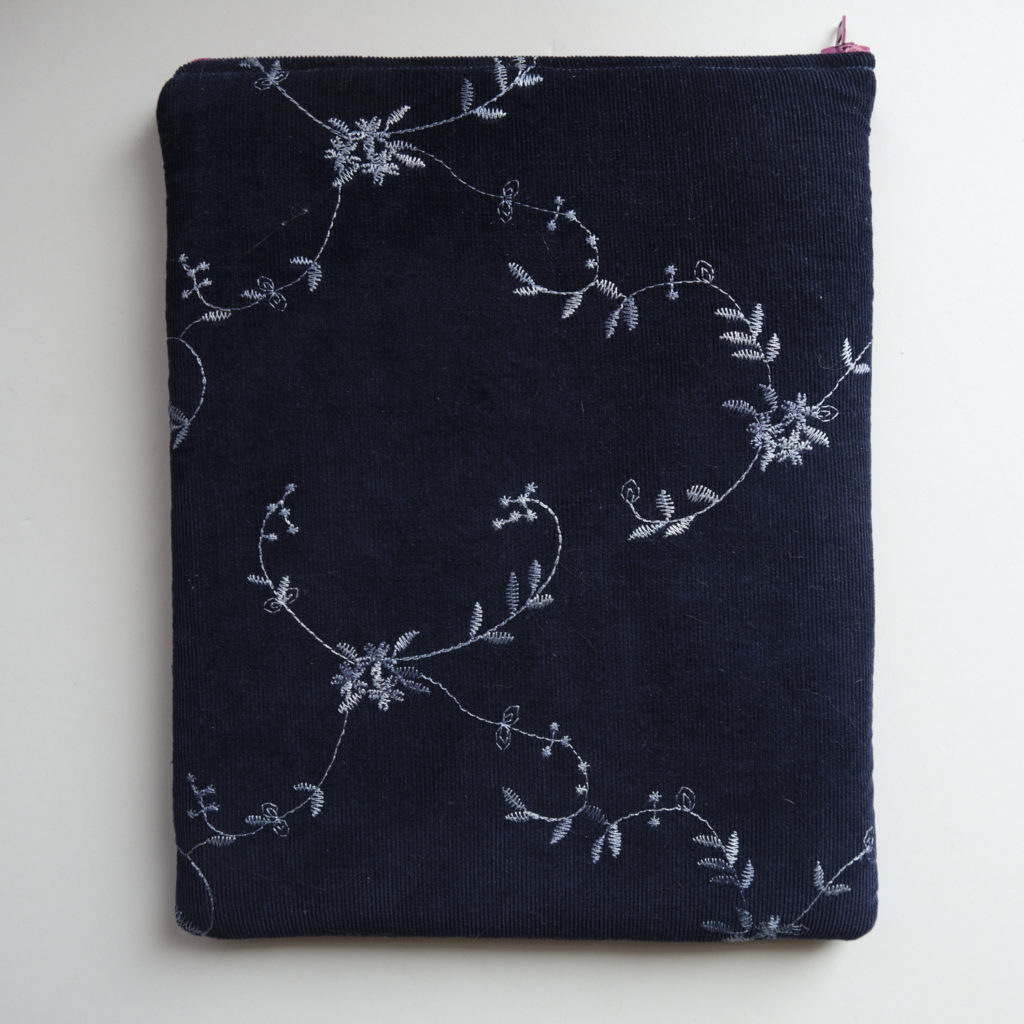 A dark blue iPad sleeve, embroidered with silver leaves. You can just see the pink accent of the zipper.