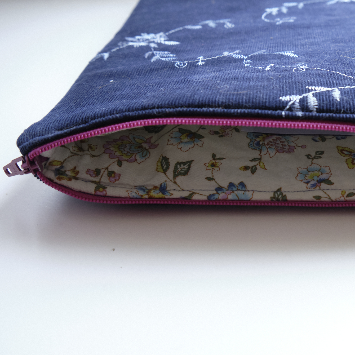 An open, dark blue iPad sleeve with a flowery lining and a pink zipper