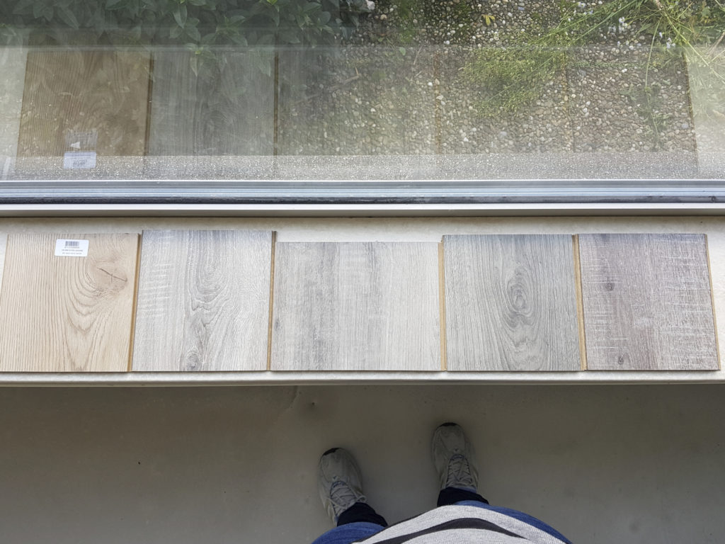 Five samples of laminate flooring. The one on the left is wood-coloured, the rest is grey.
